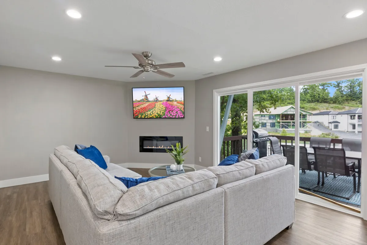 This image features a spacious interior with a large sectional sofa, a TV with colorful artwork above, a cozy fireplace, and a sliding glass door leading to a patio. Natural light pours in, highlighting the plush seating and offering views of the outdoors.