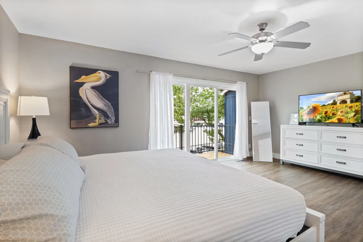 A spacious, tranquil bedroom with a large bed adorned in plush bedding, soft lighting from the bedside lamps, and tasteful artwork on the wall. Natural light filters in through the window, creating a serene environment perfect for rest and relaxation.
