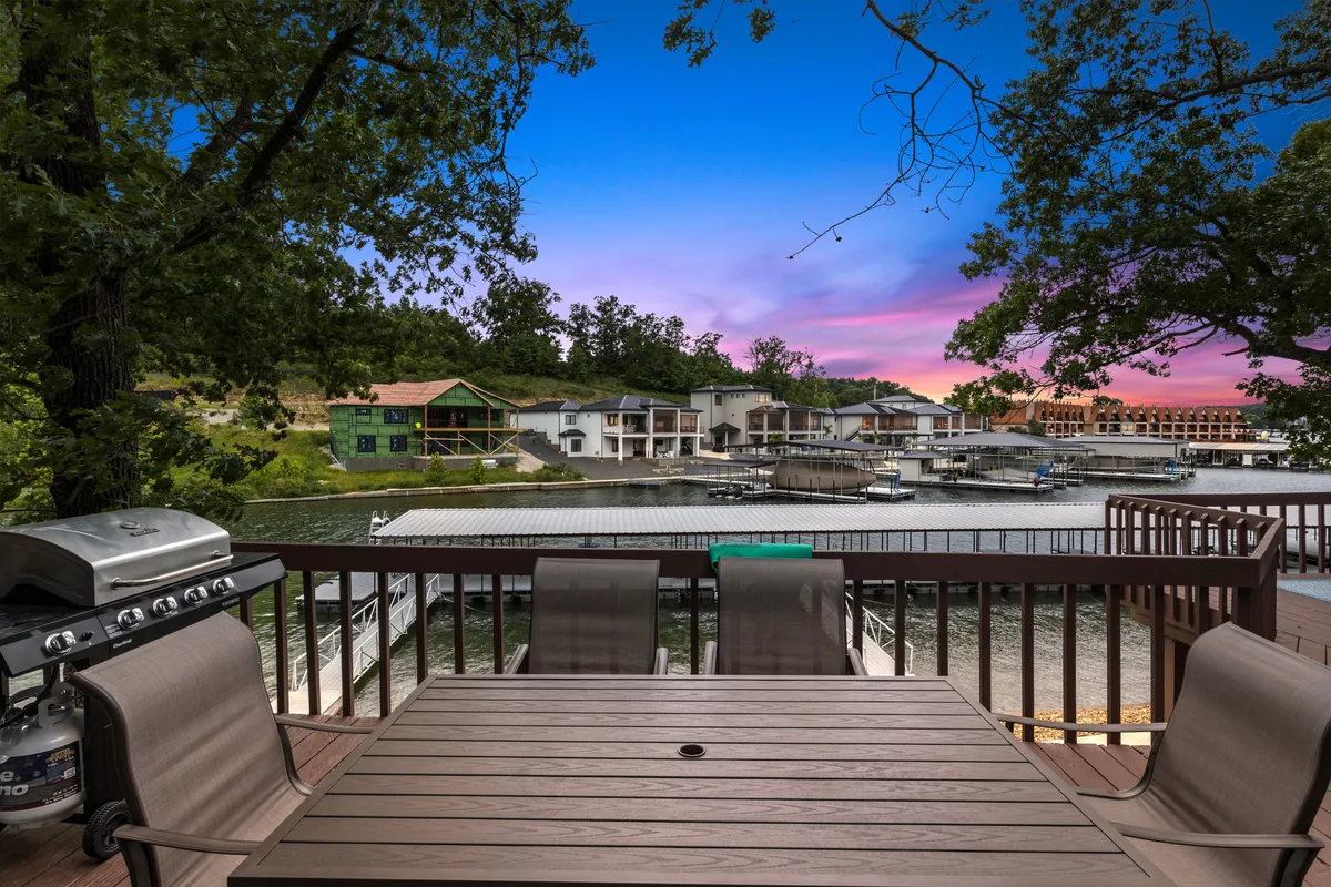 An inviting lakeside deck with a dining table, grill, and a sweeping view of the lake. The setup is ideal for social gatherings, outdoor meals, and relaxing moments overlooking the water. Houses across the lake add to the lively, communal atmosphere.