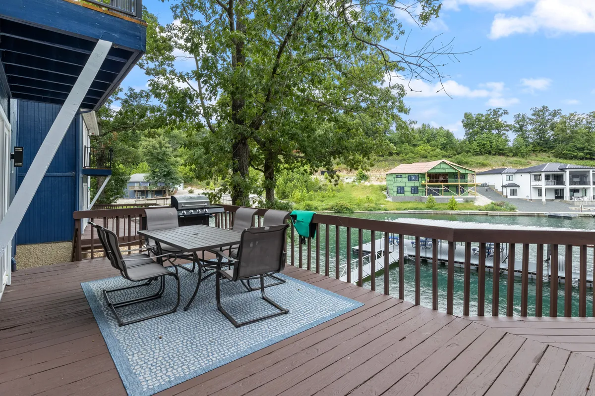The image showcases an inviting outdoor dining area set on a deck overlooking the tranquil waters of a peaceful cove, framed by lush trees. The scene suggests an ideal setting for sunset dinners, morning coffee, and social gatherings, all with serene water views and a natural backdrop.