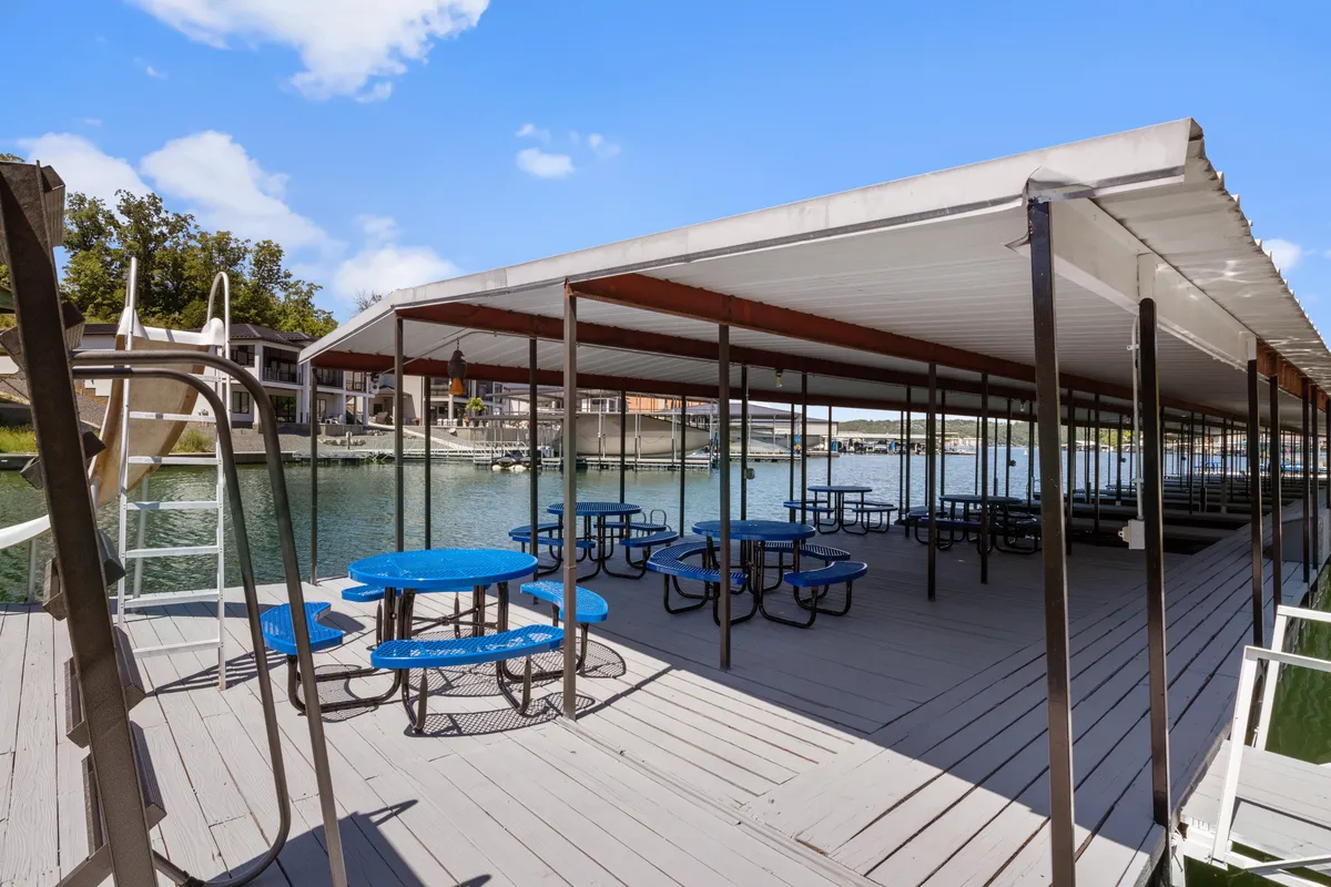 The image displays a relaxed, social dock scene with picnic tables set right by the waterfront, a dock area equipped for swimming and boating, and a ladder for easy water access. The setting is ideal for group gatherings, water activities, and watching sunsets over the lake.