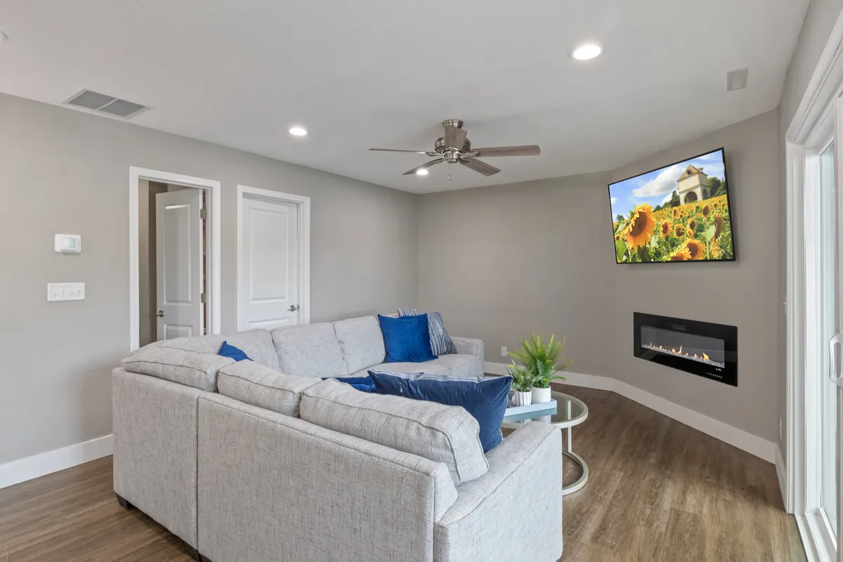 Another angle of the living area reveals a large sectional sofa with decorative pillows, a mounted TV, and a modern electric fireplace. The ambiance is cozy and contemporary, ideal for movie nights or casual socializing.