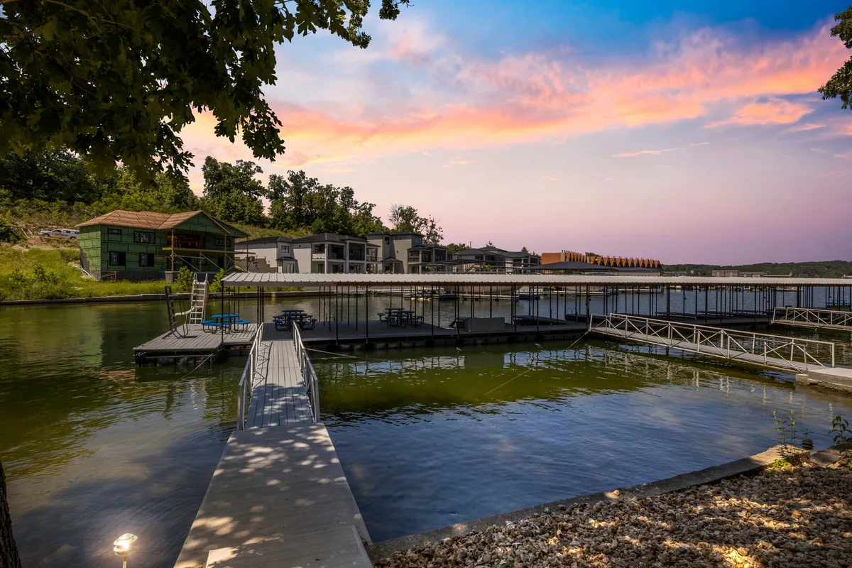 A serene view of the dock stretching over calm lake waters, surrounded by trees and nearby buildings. The dock area is inviting, with space for swimming, relaxing, and enjoying the gentle water. The tranquil setting is perfect for families seeking safe water play.