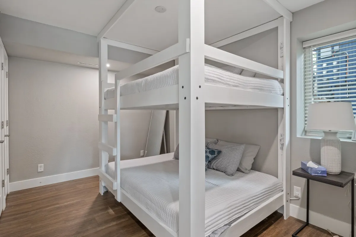 A playful and cozy bedroom with a bunk bed, decorative pillows, a bedside lamp, and wall art. The scene is inviting, suitable for families or groups, and highlights a fun, communal sleeping arrangement.