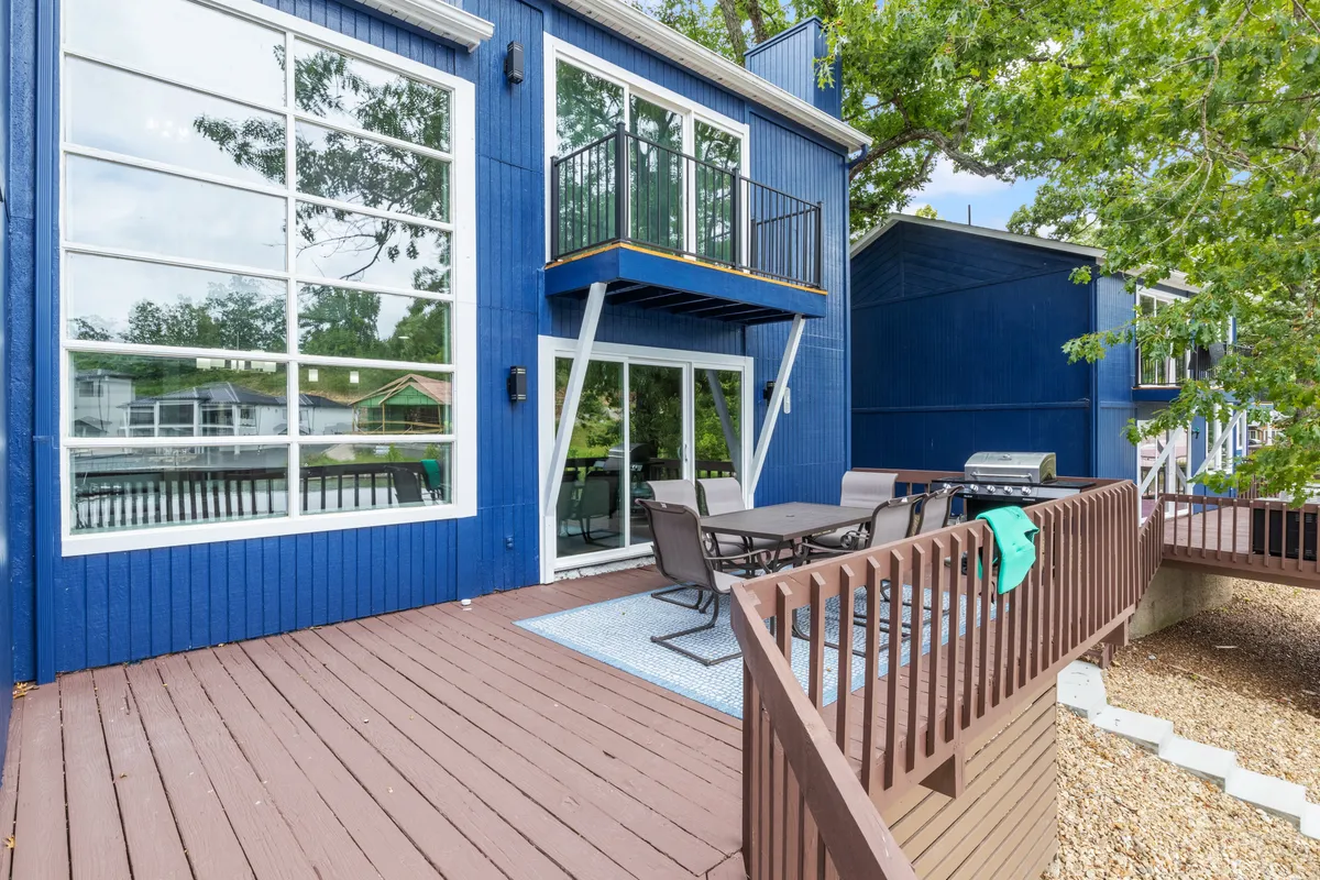 An exterior view of the property showing large windows, a blue exterior, an outdoor seating area, and an expansive deck. The scene suggests both comfort and opportunity for outdoor entertaining, with the promise of sunset views and lively gatherings.