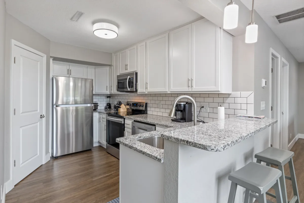 A bright, contemporary kitchen featuring granite countertops, stainless steel appliances (including a refrigerator, oven, and microwave), a spacious kitchen island with seating, and crisp white cabinetry. The space is open and inviting, designed for both cooking and socializing.