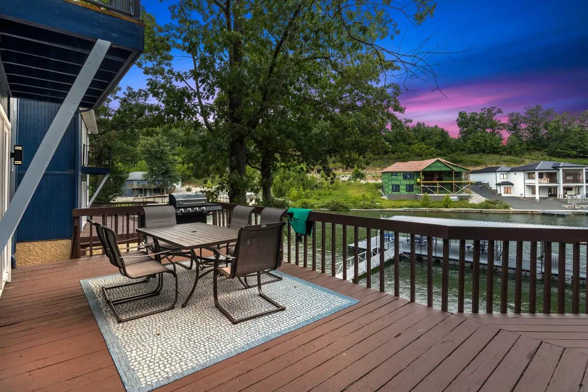 A peaceful deck area with a dining table overlooks the shimmering lake, surrounded by trees. The atmosphere is serene, with open space for relaxation, social gatherings, or simply enjoying the view after a day of adventures.