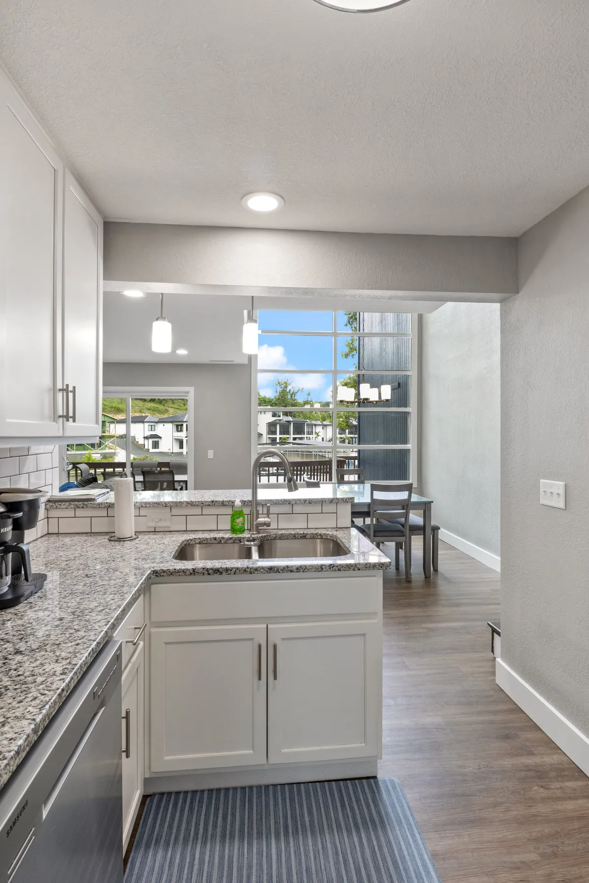 A second angle of the kitchen area, emphasizing the granite countertop with a stainless steel sink, visible kitchen appliances, and an adjacent dining area with comfortable chairs. The scene is warm and welcoming, perfect for shared meals and casual gatherings.